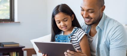 A man siting on a sofa with a girl on his lap reading.