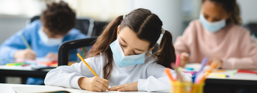 Children wearing masks and writing on notebook