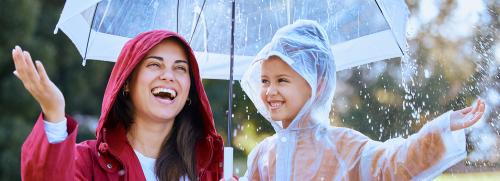 Woman and child playing under the rain with raincoats and under an umbrella