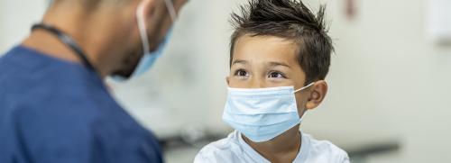 Boy wearing a face mask looking at a medical professional.