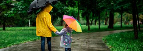 Adult and child with umbrellas under the rain.