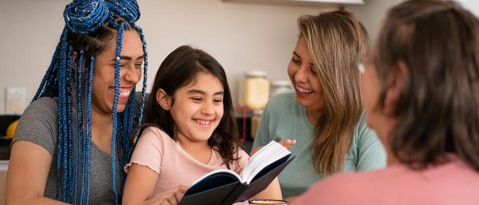 Woman sitting, laughing and reading to a child on her lap, with two other women