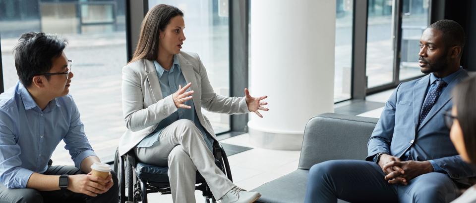 Professional woman in chair talking to two other professionals