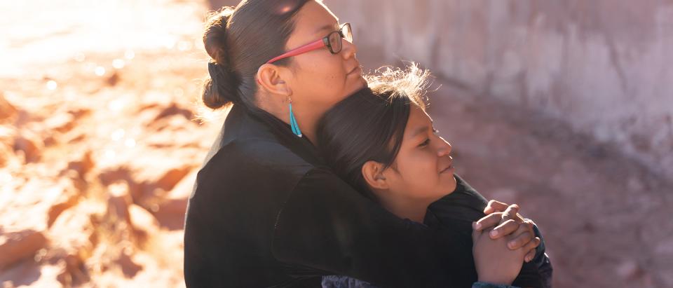 A native woman and a native girl hugging and sitting outside