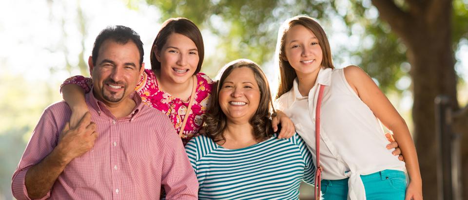 Man, woman and two female teenagers smiling outdoors