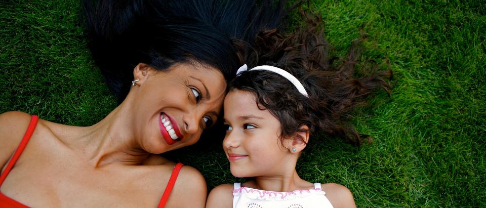 Woman and young girl lying in grass smiling at each other