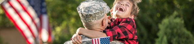 Child hugging military man while laughing and holding a flag