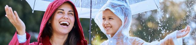 Woman and child playing under the rain with raincoats and under an umbrella
