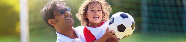 Girl being held by father while holding a soccer ball, laughing